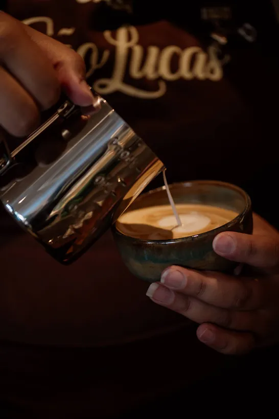 Leite vaporizado sendo servido sobre um espresso, com o letreiro São Lucas ao fundo